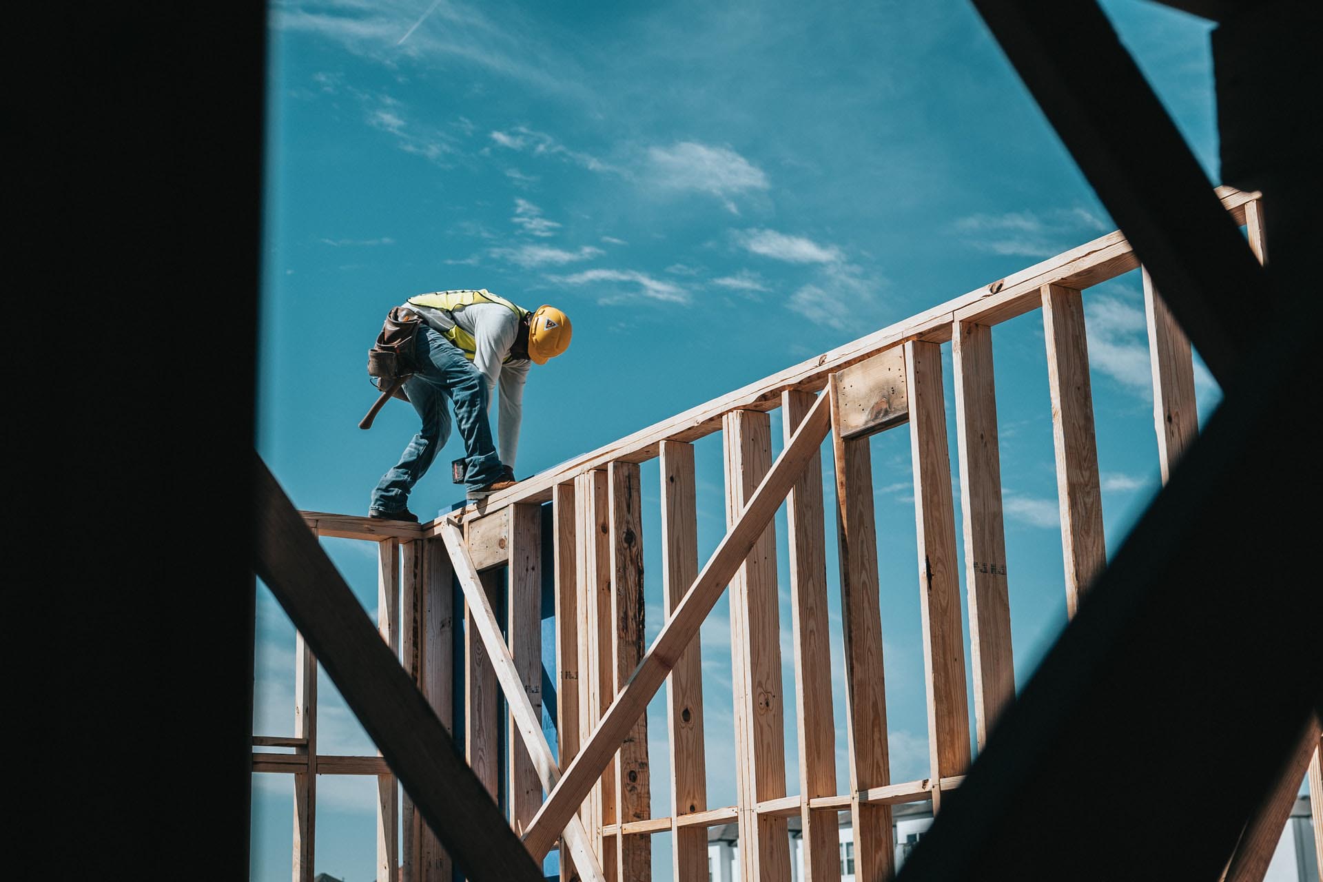 Ein Bauarbeiter steht gebückt auf einem Gerüst aus Holzbalken auf einer Baustelle