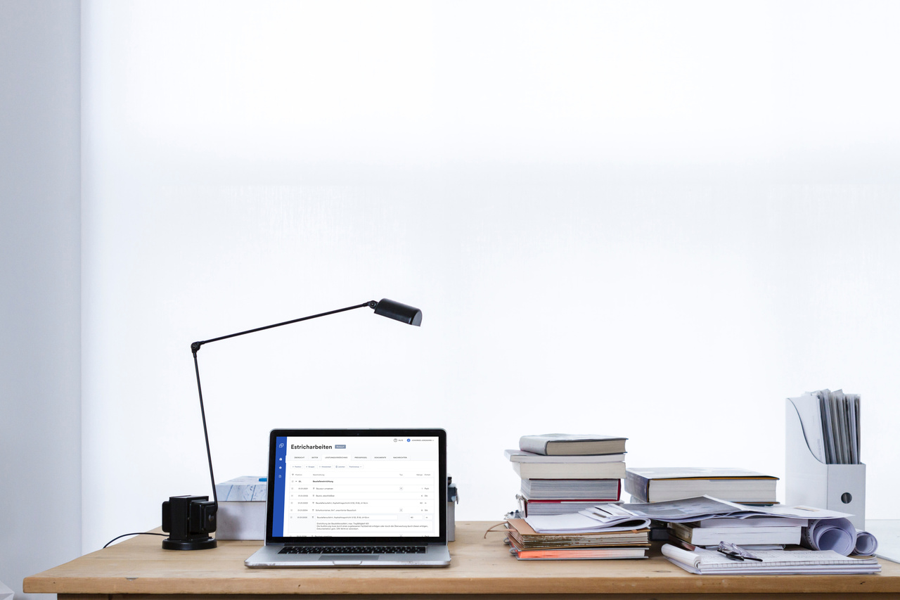 Ein Schreibtisch mit Aktenstapeln, in der Mitte steht ein Laptop, auf dem die Cosuno Software mit Leistungsverzeichnis Editor geöffnet ist